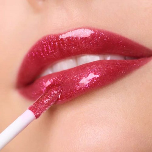 Närbild av läppar som applicerar rosa gloss med en borste på blanka läppar.