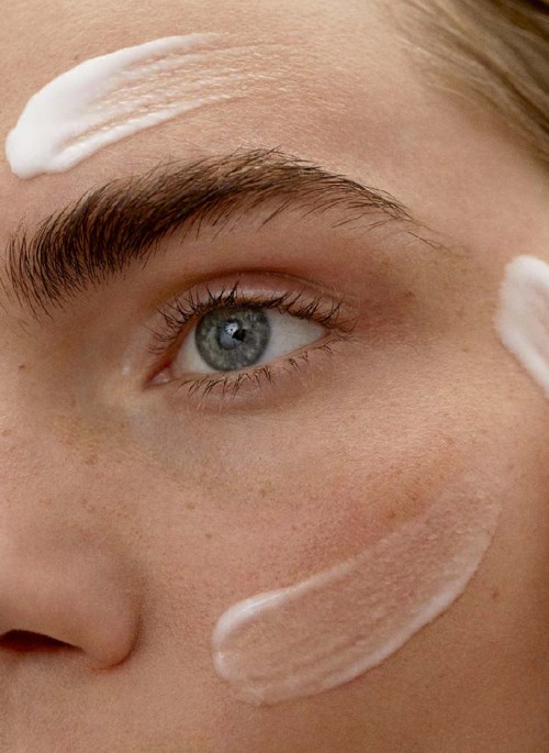 Iemand heeft crème op voorhoofd en wang, met een heldere oog en bruine wenkbrauwen.