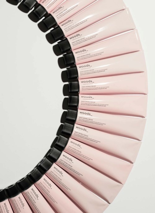 Rijen roze tubes met zwarte doppen in een gebogen patroon. De tubes hebben tekst, waarschijnlijk een schoonheidsproduct.