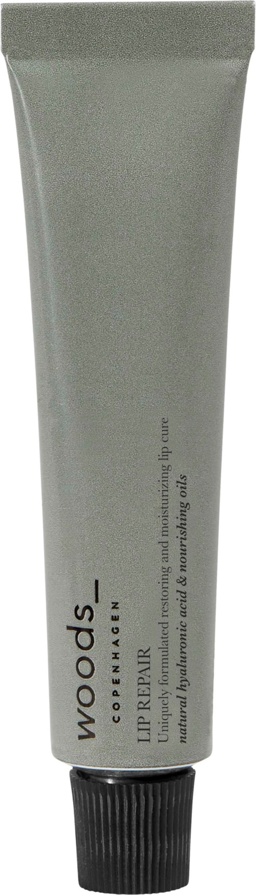 Putkilossa Woods Lip Repair huultenhoitoaine, musta kansi, harmaa pakkaukko, teksti huultenhoidosta.