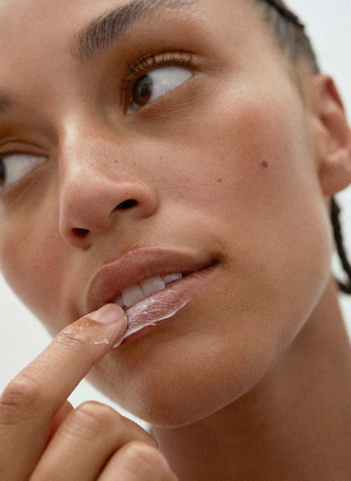 Close-up van een persoon met bruine ogen, die lippen aanrukt en een vinger op de mond heeft, kijkt zijwaarts.