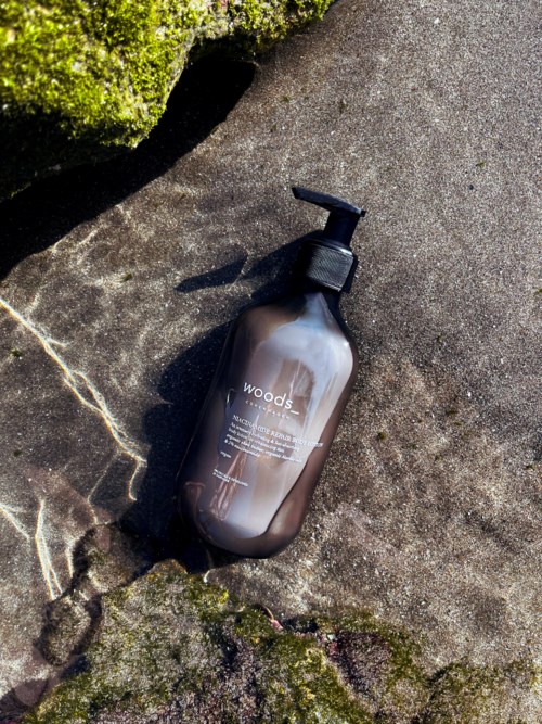 Een bruine fles met pomp op een rots, zonlicht werpt schaduw, omgeven door mos en natuurlijke omgeving.