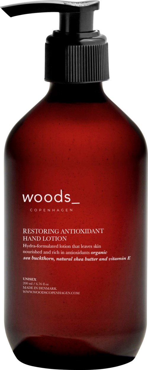 A dark red bottle with a black pump, labeled Woods Copenhagen, for hand lotion with antioxidants and organic ingredients.