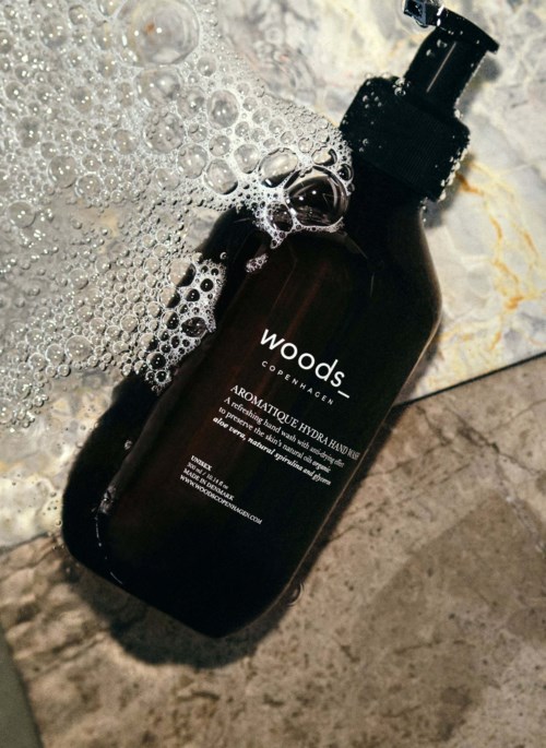 A dark brown pump bottle labeled 'wood' with soap bubbles on it, placed on a marble surface.
