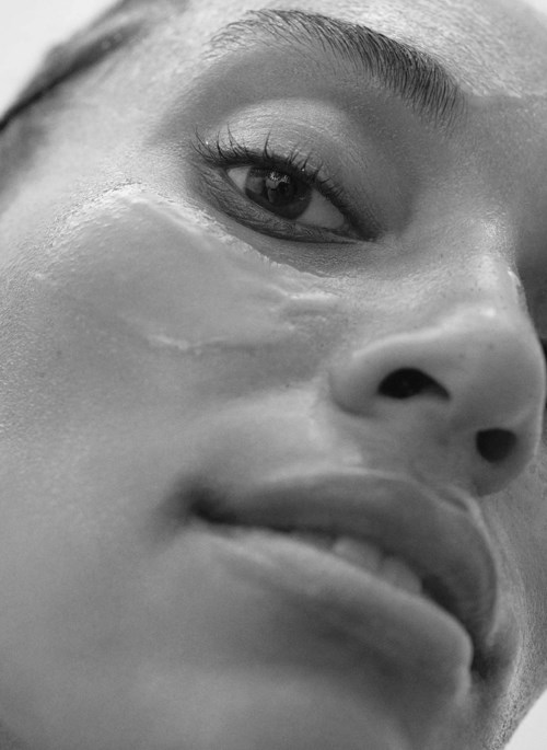 Close-up van het gezicht van een vrouw met gladde huid, donker oog, volle lippen en licht opgetrokken wenkbrauwen.