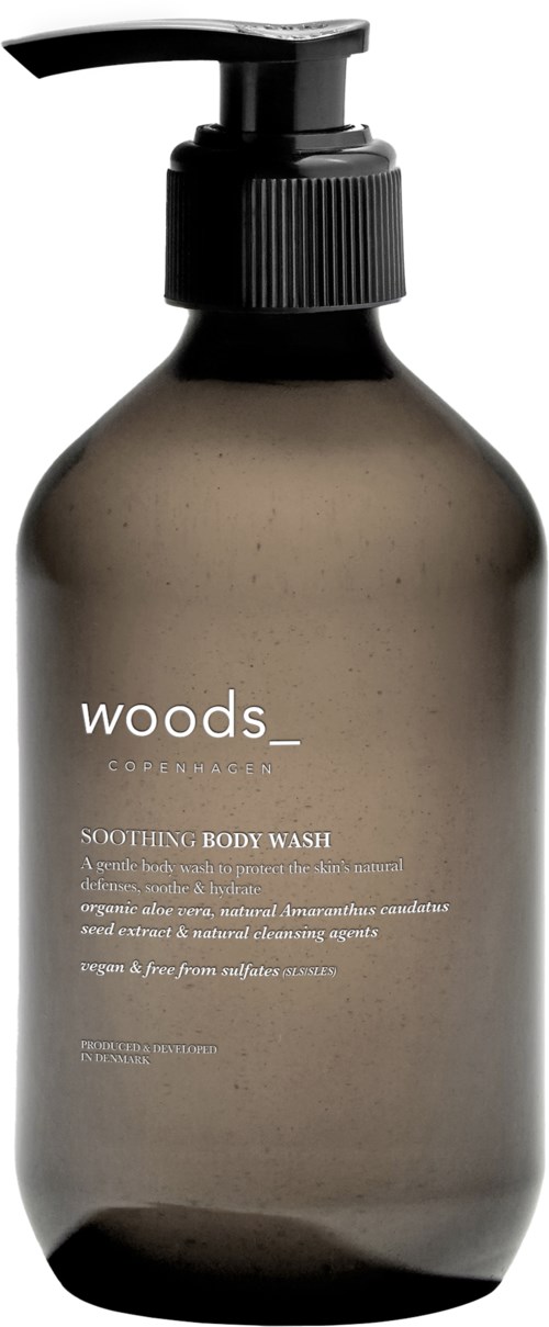Szklana szara butelka z pompką z napisem 'Woods Copenhagen' do łagodzącego mydła do ciała, prosty i elegancki design.