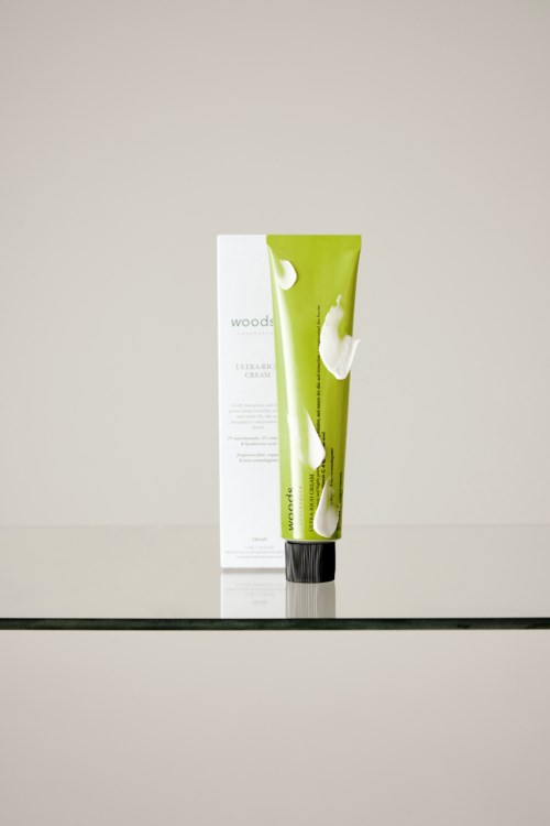 Een groene en witte tube met crème en een zwarte dop, staat op een glazen oppervlak, met een doos erachter.