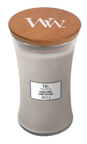 A large white candle in a glass jar with a wooden lid, labeled with the brand WoodWick and scent Sacred Smoke.