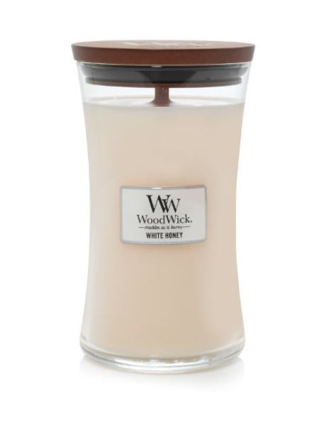 Et stearinlys i et glasskrus med trelokk, merket 'WoodWick White Honey'.