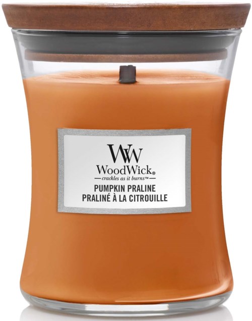 En pumpkinfärgad doftljus i en glasburk med lock av trä och en etikett som säger WoodWick, doft av pumpapralin.