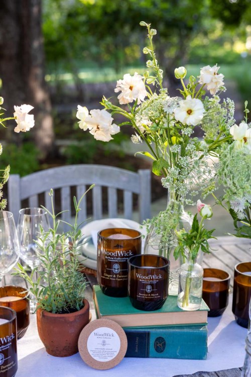 A table with flowers, candles, glasses, and a book outdoors, in a garden setting.