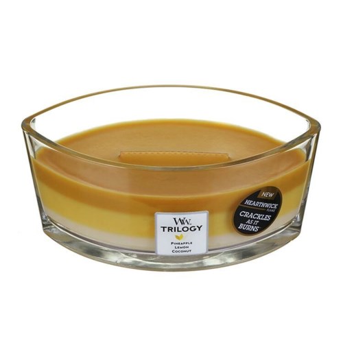 A tealight candle in a clear glass holder, with a layered yellow-orange wax design and a label listing pineapple, lemon, and coconut.