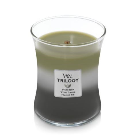 Ett ljus i glasbehållare med grönt och svart vax, märkt 'TRILOGY' och 'Evergreen Wood Scent.'