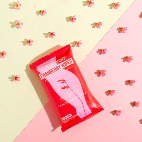 En förpackning Cranberry Wipes på en bakgrund som är delad i gul och rosa, omgiven av små rosa blommor.
