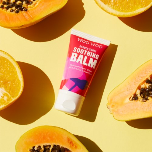 En tub med lugnande salva omgiven av skurna papayas och apelsiner på gul bakgrund.
