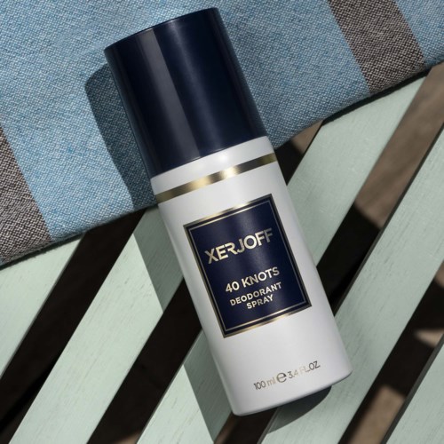 En vit deodorant sprayflaska med svart lock och guldfärgad accent, placerad på en ljus, randig yta.