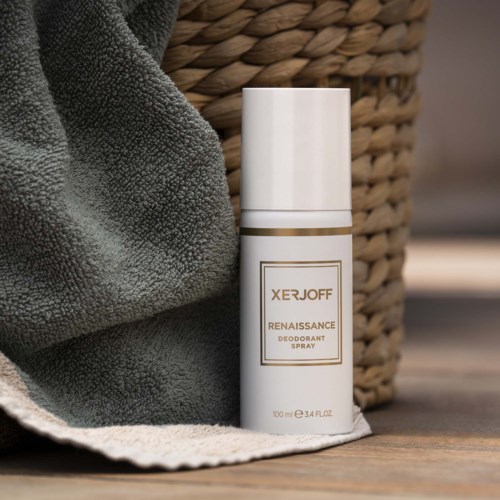 En vit deodorantsprayflaska står bredvid en grå handduk och en vävd korg.