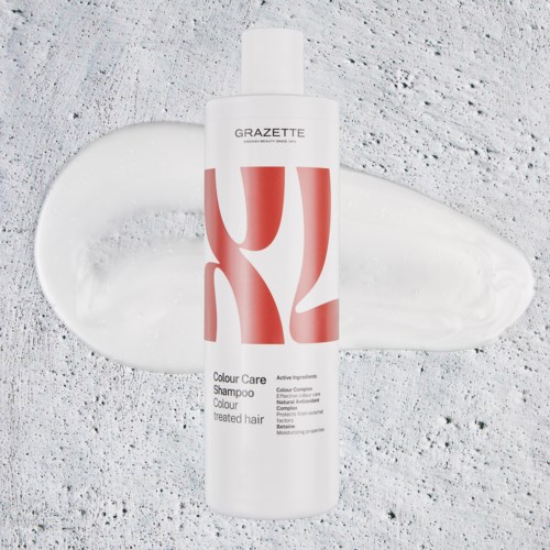 A white bottle labeled 'GRAZETTE Colour Care Shampoo' with red and black text, placed on a textured surface with some shampoo spill.