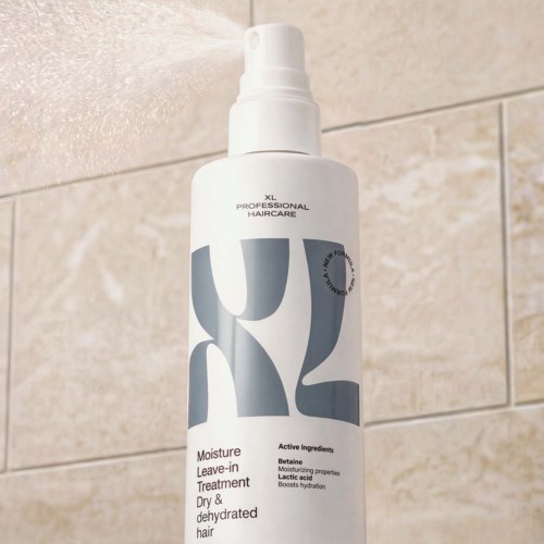 Vit sprayflaska för hårvård med XL Professional Haircare-logga och text, mot beige kakelbakgrund.