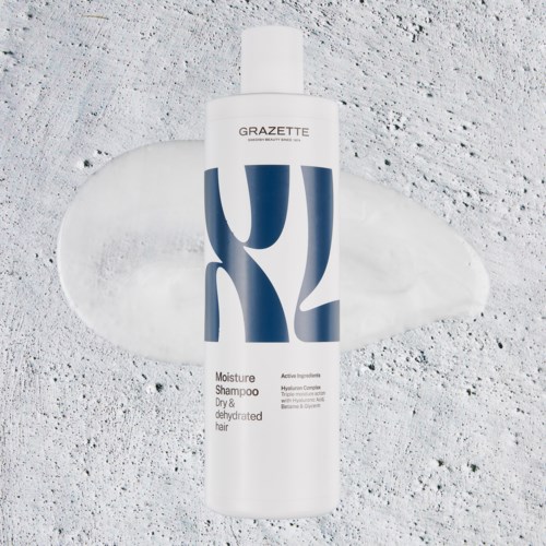 A white bottle with blue and black text labeled Grazette, placed on sandy surface with cream spill.