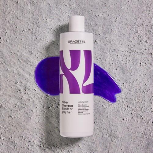 Een witte fles zilvershampoo met paarse ontwerp, op een gestructureerde grijze ondergrond.