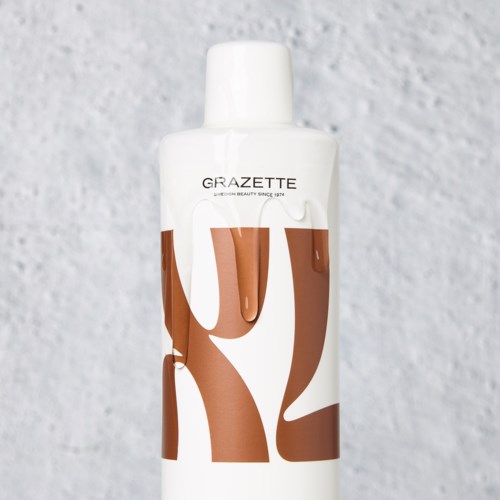 A white bottle with brown and white text, standing against a textured gray background.