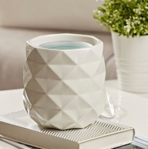 En vit texturerad keramikmugg på en stängd bok, med en liten blomkruka i bakgrunden.