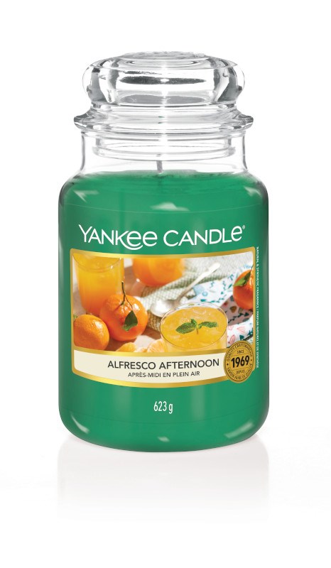 A green Yankee Candle jar with a label showing oranges and a yellow drink, labeled 'Alfresco Afternoon'.