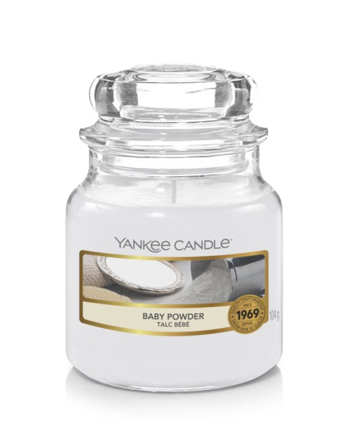 Ett klart glasburk med lock, märkt Yankee Candle Baby Powder, med ett gyllene märke som visar 1969, och en bild av ett pulverapplikator.