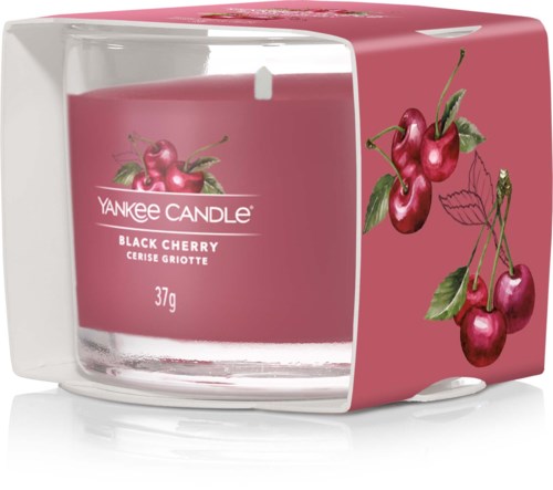 Ett rosa ljus i ett glas med körsbärsillustrationer på förpackningen.