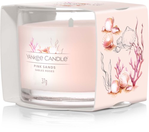 En pink doftljus med snäckor och koraller, märkt 'Pink Sands' i ett tydligt glas.