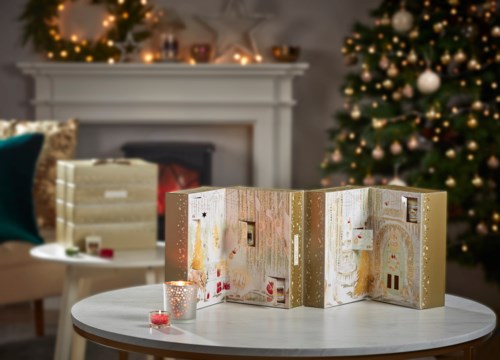 En julscen med pyntade julgranar, en tänd öppen spis och en festlig adventskalender på ett bord.