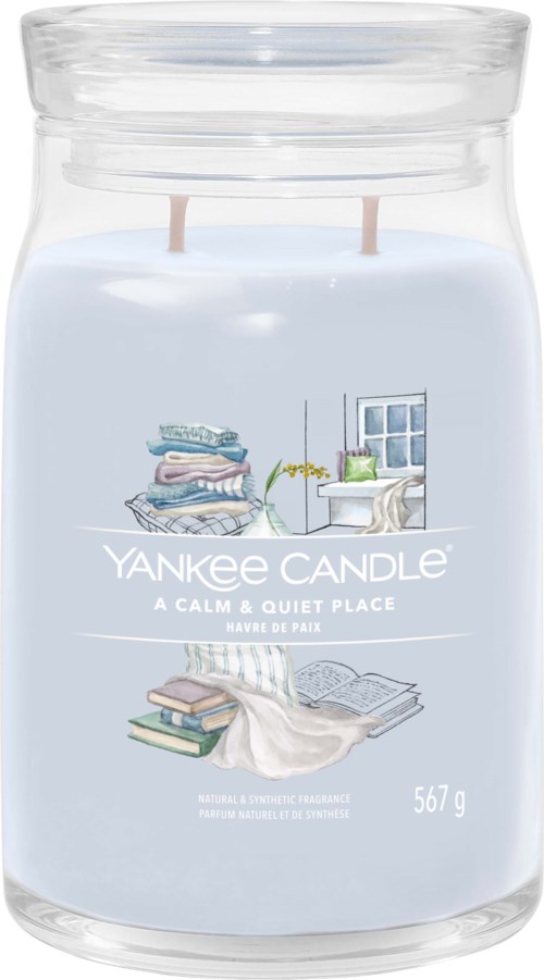 Eine blaue Yankee Candle-Glasvase mit einem Etikett, das einen gemütlichen Raum mit Büchern, Fenster und Pflanze zeigt.