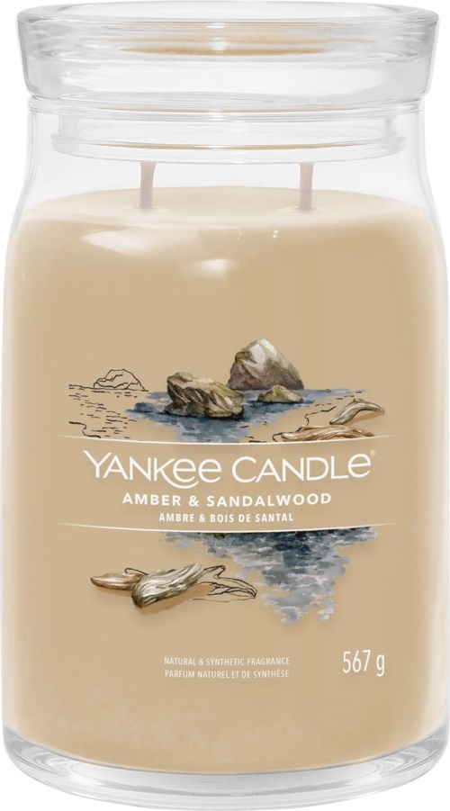 Een kaars in een glazen pot met zandkleur, met stenen en water ontwerp, gelabeld Yankee Candle Amber & Sandalwood.