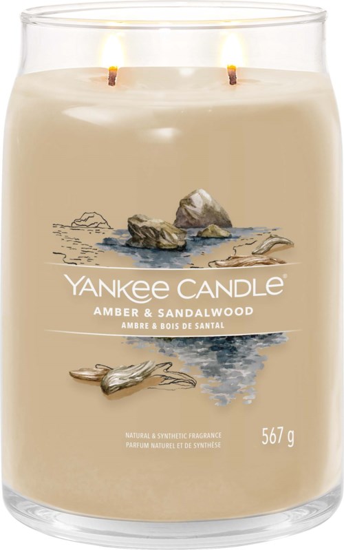 Een kaars in een glazen pot met twee lonten, met label 'Yankee Candle Amber & Sandalwood,' met een strandtafereel.
