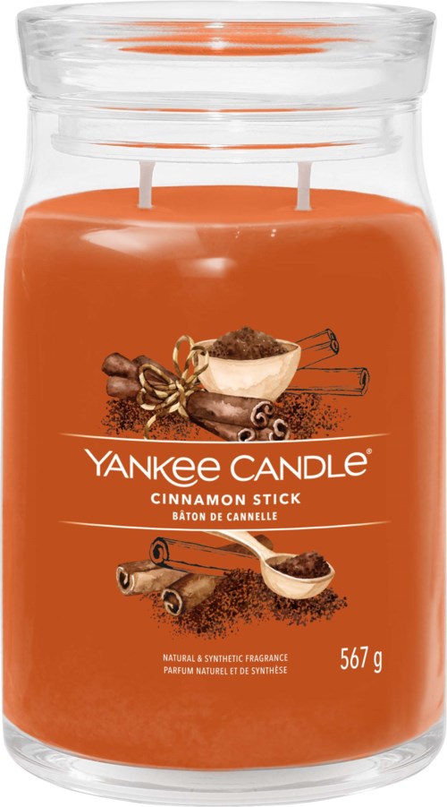 Duży pomarańczowy świecznik zapachowy z dwoma knotami, oznaczony Yankee Candle Cinnamon Stick.