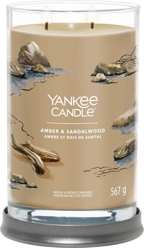 Ett stort glasljus med beige vax, berg, trä och vatten illustrationer, märkt Yankee Candle Amber & Sandalwood.