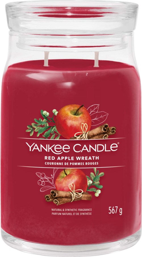 A large red candle in a glass jar labeled Yankee Candle, with apple and cinnamon decorations, weighing 567 grams.
