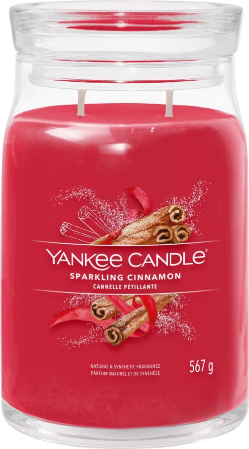 A red candle in a glass jar with cinnamon sticks and a red ribbon on the label.