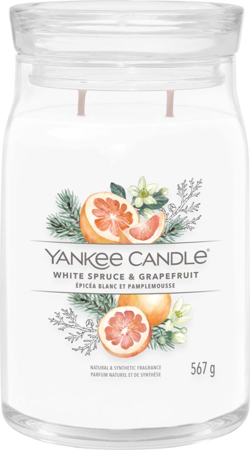 A clear candle jar with a label showing white spruce, grapefruit, and decorative greenery and flowers.