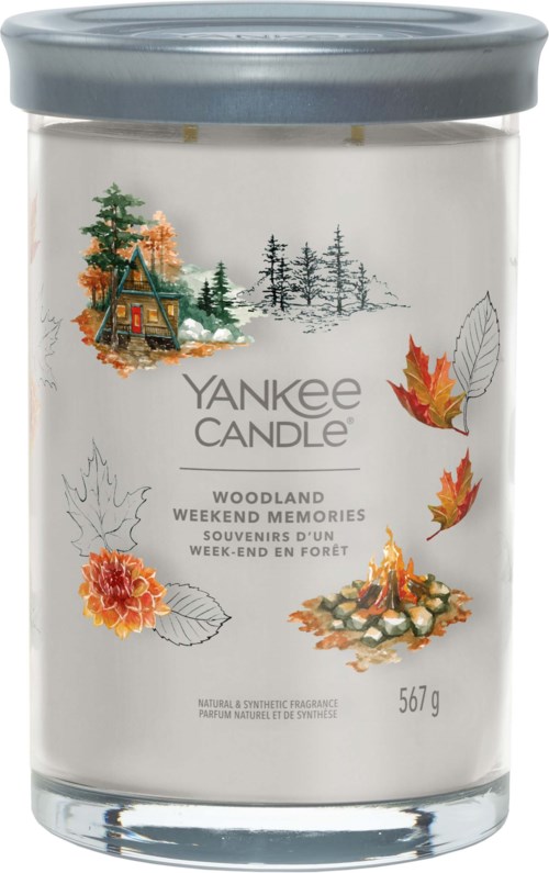 A Yankee Candle with autumn leaves, pine trees, a small house, and a campfire on a white background.