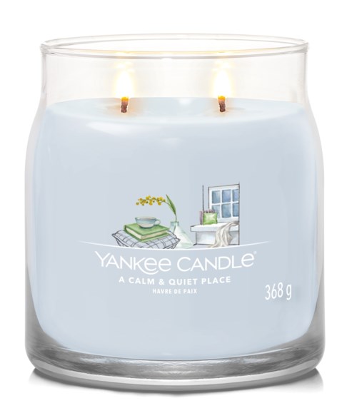Eine brennende Yankee Candle mit hellblauer Etikette, zeigt eine gemütliche Raumszene und den Text 'A CALM & QUIET PLACE.'