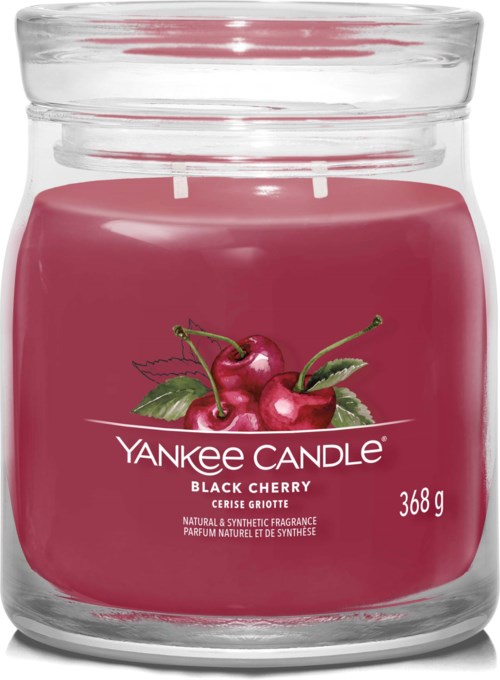 Et rosa duftlys i glasskrukke med kirsebær og grønne blader på etiketten. Det er et Yankee Candle med kirsebærduft.