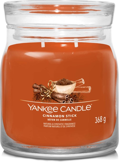 Et glasslys med oransje etikett med kanelstenger og krydder, merket Yankee Candle Cinnamon Stick.