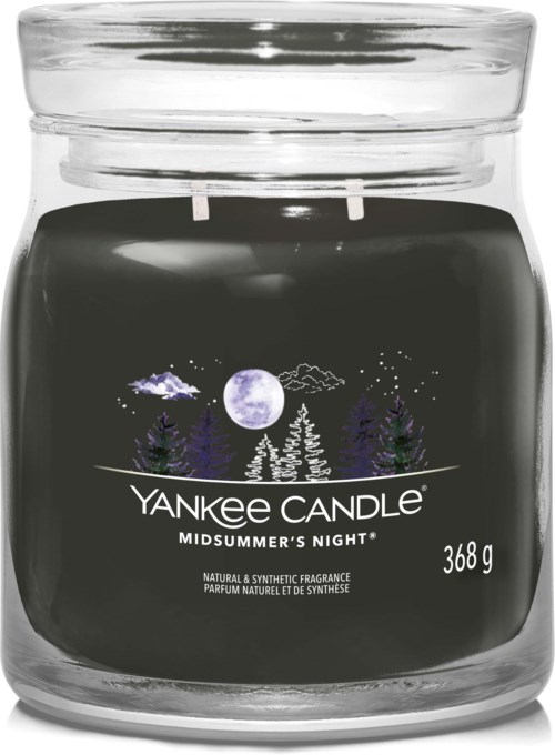 Czarna świeca zapachowa w szklanym słoju z białymi i fioletowymi drzewami, księżycem i gwiazdami, z etykietą 'Yankee Candle Midsummer's Night' i wagą.