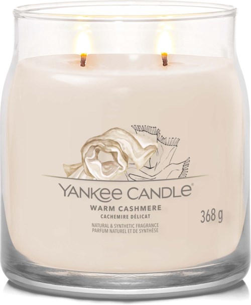 Biały świeca w przezroczystym szklanym pojemniku z dwoma palącymi się knotami, oznaczona 'Yankee Candle', zapach to ciepły kaszmir.