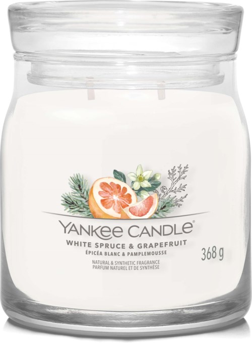 A white candle in a glass jar with a label showing grapefruit and white spruces. It is a Yankee Candle.