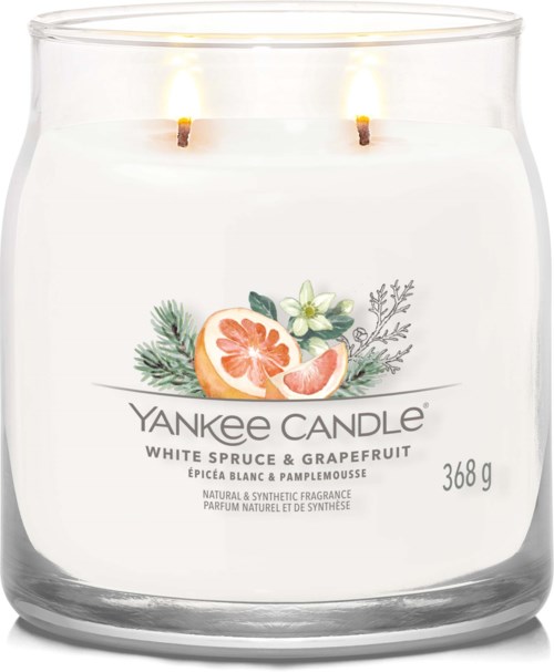 A white scented candle in a glass jar with a grapefruit and green leaves on the label, two wicks are lit.