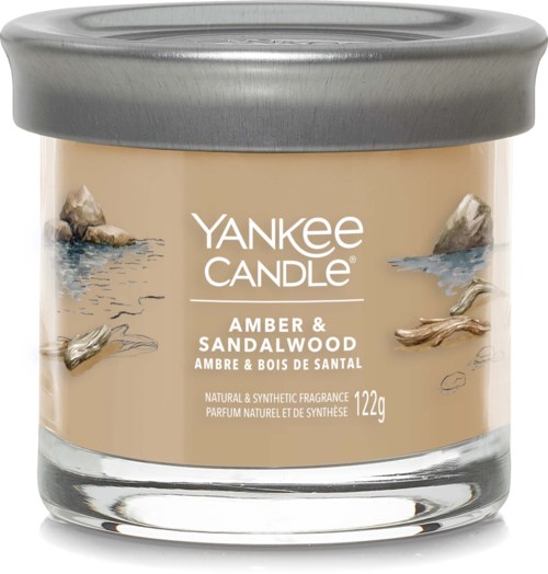 En Yankee Candle-kruka med silverlock, märkt doft av bärnsten och sandelträ, väger 122g, med bilder av stenar och vatten.