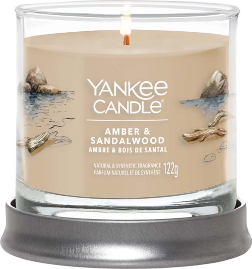 Ett doftljus i glasbehållare med stenar och vatten, märkt som Yankee Candle Amber & Sandalwood doft.